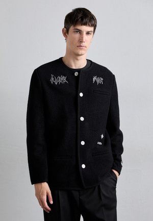 Schwarze Wollmischungjacke mit silbernen Knöpfen, runder Ausschnitt, seitlichen Taschen und grafischer Stickerei auf der Vorderseite und dem Ärmel.