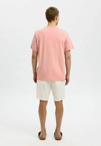 Rosa bomullströja med korta ärmar, avslappnad passform och rundad halsringning, i kombination med vita shorts och mörka sandaler.