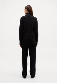 Maglione nero a collo alto con coste e spalle basse, abbinato a pantaloni neri a gamba larga. L'outfit presenta una vestibilità comoda e dettagli minimi.