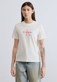 Μπεζ βαμβακερό t-shirt με κοντά μανίκια, με έντονο κόκκινο και μπλε λογότυπο "Calvin Klein" στο κέντρο του στήθους.