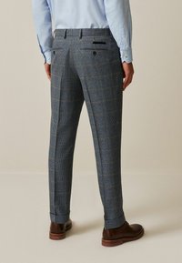 Tailored trousers in houndstooth pattern; blue-gray fabric with yellow accents; rear pockets, slim fit, cuffed hem, paired with brown shoes.