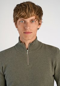 Grüner Reißverschluss-Pullover mit strukturiertem Strickmuster und hohem Kragen, ausgestattet mit einem silbernen Reißverschluss und einer taillierten Passform.