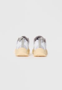 White sneakers with a textured upper, gray accents, and a beige rubber sole. Features a pull tab on the heel for easy wear.