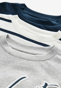 Tre t-shirts med rund hals: marineblå, hvid med marineblå striber og grå. Hver har ribbede halsudskæringer og blød bomuldsstruktur.