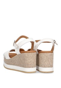 Sandalias de cuña blancas con un tacón de tela beige texturizada. Cuentan con correas ajustables en el tobillo y una plantilla marrón suave.