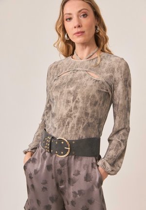 Top de manga larga en tejido gris texturizado con detalles recortados, combinado con pantalones grises de tiro alto con un patrón de hojas y un cinturón negro.