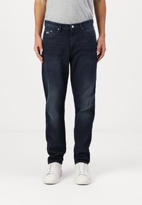 Mørkeblå denim jeans med rett passform, med et tradisjonelt fem-lommersdesign og knappelukking, kombinert med hvite sneakers.