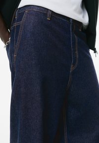 Donkerblauwe denim jeans met contrasterende oranje stiksels, voorzien van een klassieke vijf-pocketontwerp en een soepele textuur.