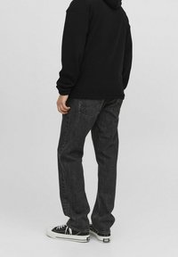 Zwarte hoodie gedragen met donkergrijze jeans en zwarte sneakers. De jeans heeft achterzakken en een rechte pijpdesign. Zachte stofstructuur.