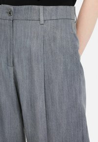 Light gray trousers made of textured fabric, featuring a button closure, front pleats, and side pockets for functionality.