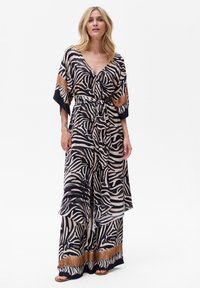 Długa, zwiewna sukienka z lekkiego materiału z wzorem w zebra w kolorze kremowym i czarnym, z brązowym akcentem na dolnej krawędzi i rękawach.