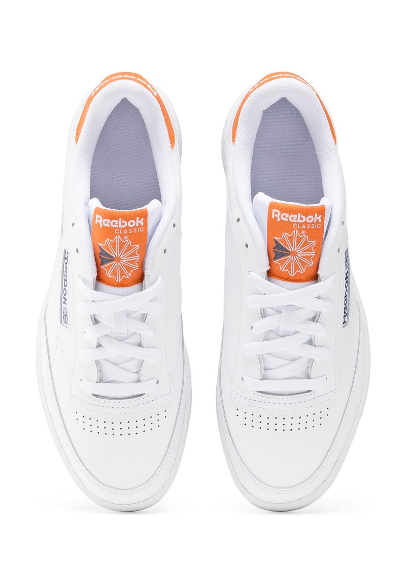 Zapatillas de cuero blancas con caja de dedos perforada. Presentan una etiqueta de logo naranja en la lengüeta y un sutil branding en los lados. Cuerdas planas blancas y cuello acolchado.