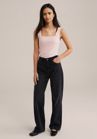 Top sin mangas de color rosa claro con escote cuadrado, combinado con vaqueros negros de tiro alto y holgados, y bailarinas negras. Conjunto simple y casual.