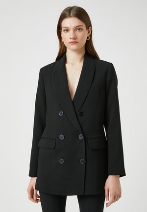 Black double-breasted blazer with notched lapels, featuring two front pockets and six large buttons, made of a smooth fabric.