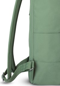 Sac à dos en tissu vert avec bretelle rembourrée et réglable ainsi qu'une boucle métallique sur fond blanc.
