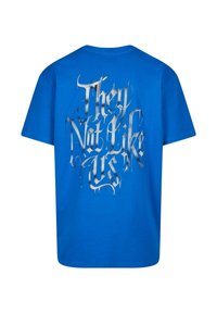 Blå bomulds t-shirt med et stort sølv grafisk tekstdesign, der står "De kan ikke lide os" på ryggen med en dryppende effekt.