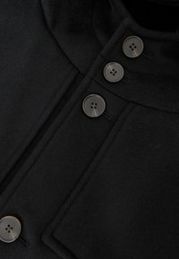 Juodas vilnonis paltas su aukštu apykakliu, turintis keturis apvalius pilkus mygtukus, slėptą užsegimą ir lygią tekstūrą bei minimalistinį dizainą.