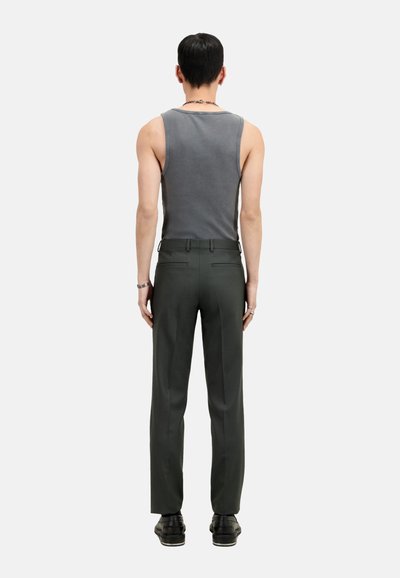 Graues Tanktop, figurbetont, kombiniert mit dunkelgrüner, taillierter Hose, gerader Schnitt, glatte Textur. Modell mit dem Rücken zur Kamera, trägt schwarze Schuhe.