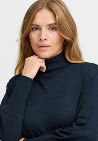 Temno mornarsko modra turtlenecka jopica iz mehkega pletenega materiala, ki ima dolge rokave in prilegnjeno silhueto. Minimalističen dizajn brez vzorcev.