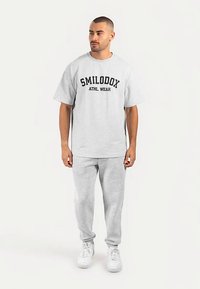 Grå oversize t-shirt med "SMILODOX ATHL. WEAR" tryckt i svart. Kombinerad med matchande gråa sweatpants och vita sneakers.