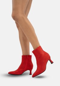 Botines rojos con superficie texturizada, que cuentan con un cremallera lateral, punta afilada y un pequeño tacón cónico. El patrón está adornado con pequeños tachuelas.