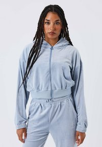 Felpa blu chiaro in velluto con zip, dotata di cappuccio regolabile, polsini a coste e pantaloni coordinati, caratterizzati da sottili dettagli in strass.