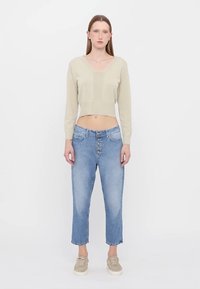 Světle zelený pletený cropped svetr s V-výstřihem, v kombinaci se světle modrými vysokými džíny s knoflíkovým zapínáním a pěti kapsami.