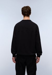 Black sweatshirt with a crew neck, ribbed cuffs, and a textured shoulder seam, paired with black cargo pants, viewed from the back.