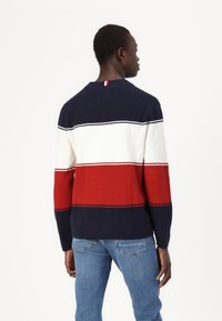 Pull bleu marine, blanc et rouge à rayures avec texture côtelée. Encolure ronde et bandes horizontales contrastantes. Manches longues, coupe décontractée.