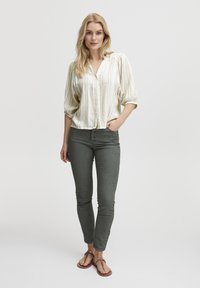 Blusa de rayas claras con mangas abullonadas, combinada con unos jeans ajustados verde oscuro y sandalias planas marrones con detalle de cadena.