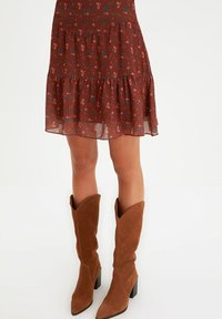 Vestido floral marrón con diseño en capas, tela transparente y dobladillo con volantes. Combinado con botas altas de ante de color tostado, con punta afilada y tacones de bloque.