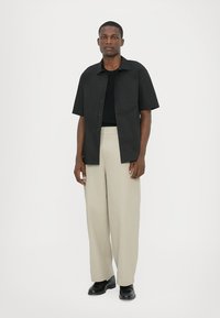 Short-sleeve black shirt with a buttoned front, paired with light beige wide-leg trousers. Black shoes complete the outfit.