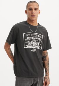 T-shirt noir en coton pour homme avec un graphique vintage du logo blanc Levi Strauss, représentant des chevaux et du texte, col rond, coupe décontractée et manches courtes.