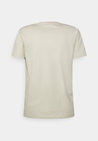 Ljus beige t-shirt med kort ärm i bomull, med rund halsringning och en slät textur. Inga synliga logotyper eller mönster.