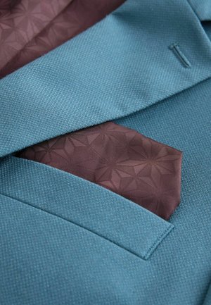 Blå tekstureret blazerlomme med et foldet brunt mønstret lommetørklæde.