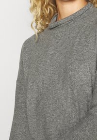 Szary, lekki, długi rękaw pulower z podwyższonym kołnierzem, charakteryzujący się teksturowanym splotem i lekko luźnym krojem. Brak widocznych wzorów lub akcentów.