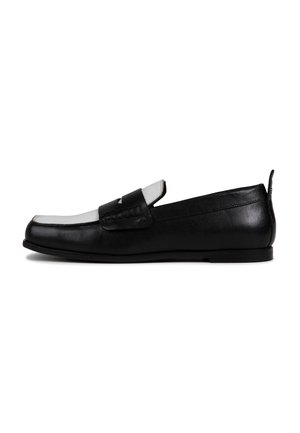Mocassins en cuir noir avec une finition lisse, un design à enfiler, un accent blanc contrastant sur le bout, et une semelle en caoutchouc de profil bas.