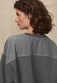 Grijze sweatshirt met een relaxte pasvorm, raglansmouwen en een contrasterend lichtergrijs paneel op de rug. Zachte textuur.