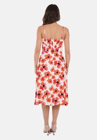 Abito estivo floreale con spalline sottili, caratterizzato da una base bianca e vivaci motivi floreali rossi, rosa e neri. Dettaglio smock sul retro. Lunghezza fino alle ginocchia.