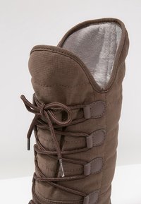 Brązowy pikowany but z miękkim, jasnoszarym wnętrzem, posiadający wiązanie oraz wzmocnione oczka po bokach.