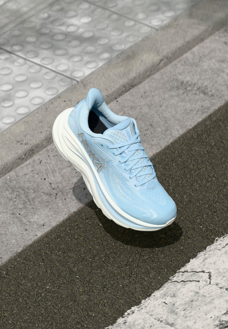 Gaiši zils sporta apavs ar elpojošu acu audumu augšdaļu, mīkstu zoli un atstarojošu sudraba zīmola logo sānos.