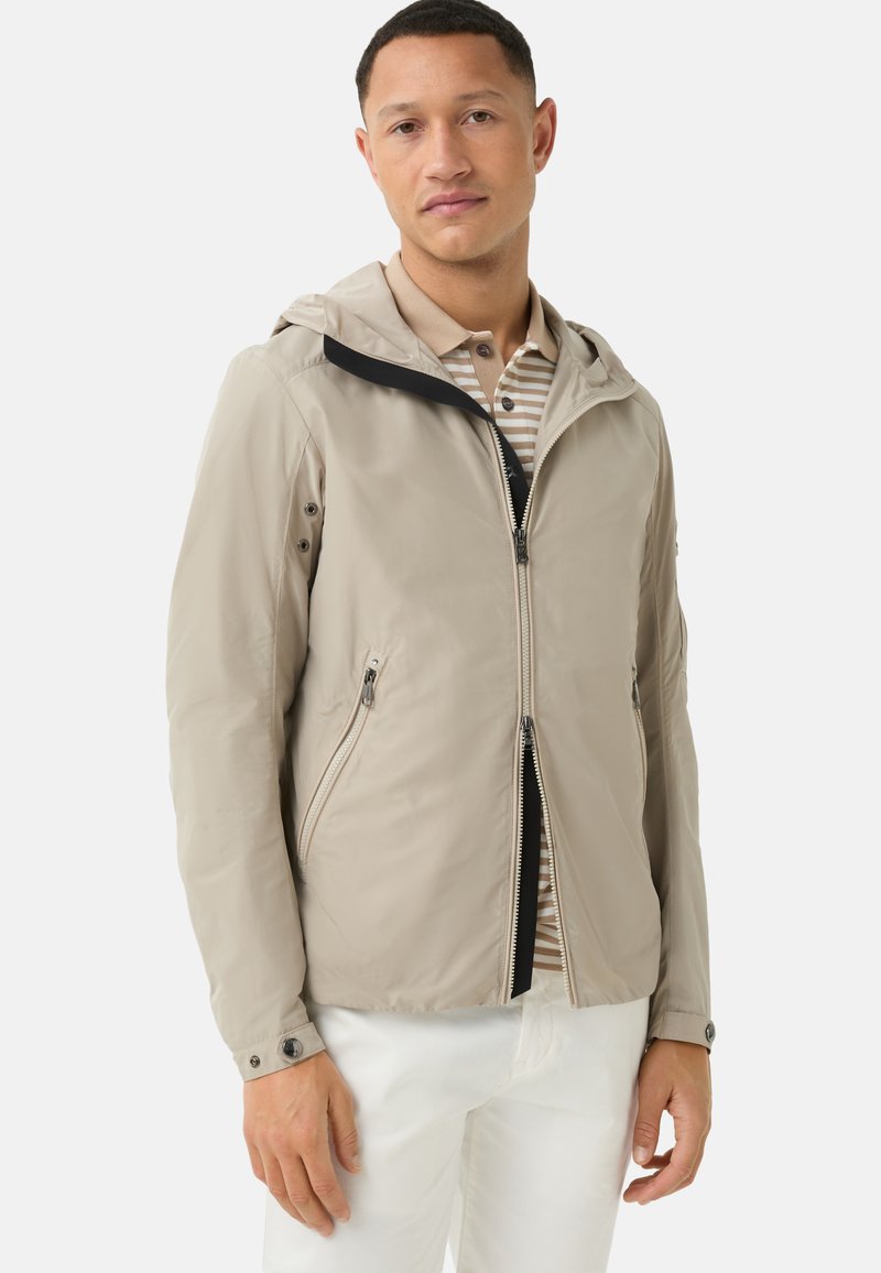 Lightweight beige jacket with a hood, zip closure, two side pockets, and black accents on the collar; smooth, water-resistant fabric.