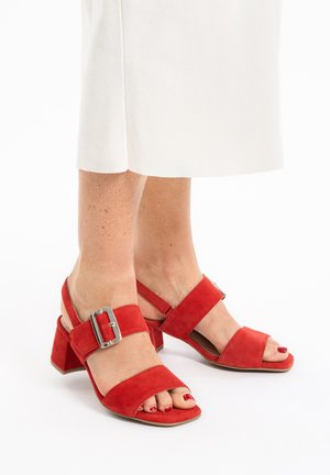 Rote Wildleder-Sandalen mit Blockabsatz verfügen über breite Riemen, ein metallisches Schnallen-Detail und ein offenes Zehendesign, kombiniert mit einem hellen Rock.