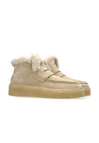 Beige suede ankle boots with a plush fur lining, moccasin stitching, and a textured rubber sole. Secure strap detail on each side.
