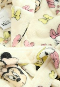 Koc polarowy z kremowym tłem i kolorowymi wzorami Minnie Mouse oraz kokardek w odcieniach różu, żółci i czerni. Miękka tekstura.
