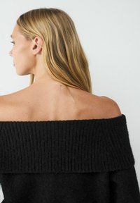 Schwarzer schulterfreier Pullover mit geripptem Ausschnitt, weicher Textur und lockerer Passform, der eine klare Rückansicht zeigt.