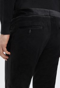 Schwarze Wildlederhose mit glatter Textur, ausgestattet mit Seitentaschen, einer Gesäßtasche mit Knopf und einem schmal geschnittenen Design.