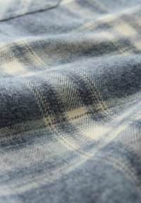 Tela de cuadros azul y crema con una textura suave, que presenta un patrón de pata de gallo. El material parece ligeramente arrugado y difuso.