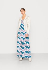 Vestido maxi com padrão abstrato colorido em azul, rosa e branco, combinado com uma jaqueta de motoqueiro ajustada branca em couro. Botas brancas até o tornozelo.