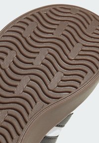 Zbliżenie na brązową podeszwę buta z wypukłymi falistymi rowkami i teksturowanymi prostokątnymi wzorami chwytu zapewniającymi przyczepność.